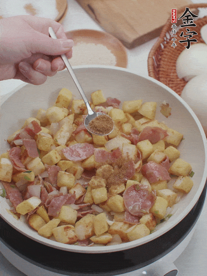 起鍋少油，煸香洋蔥丁、蔥白，加入金字培根火腿翻炒幾下，再加入饅頭丁、1小勺孜然粉、少許鹽翻炒均勻并鋪平。